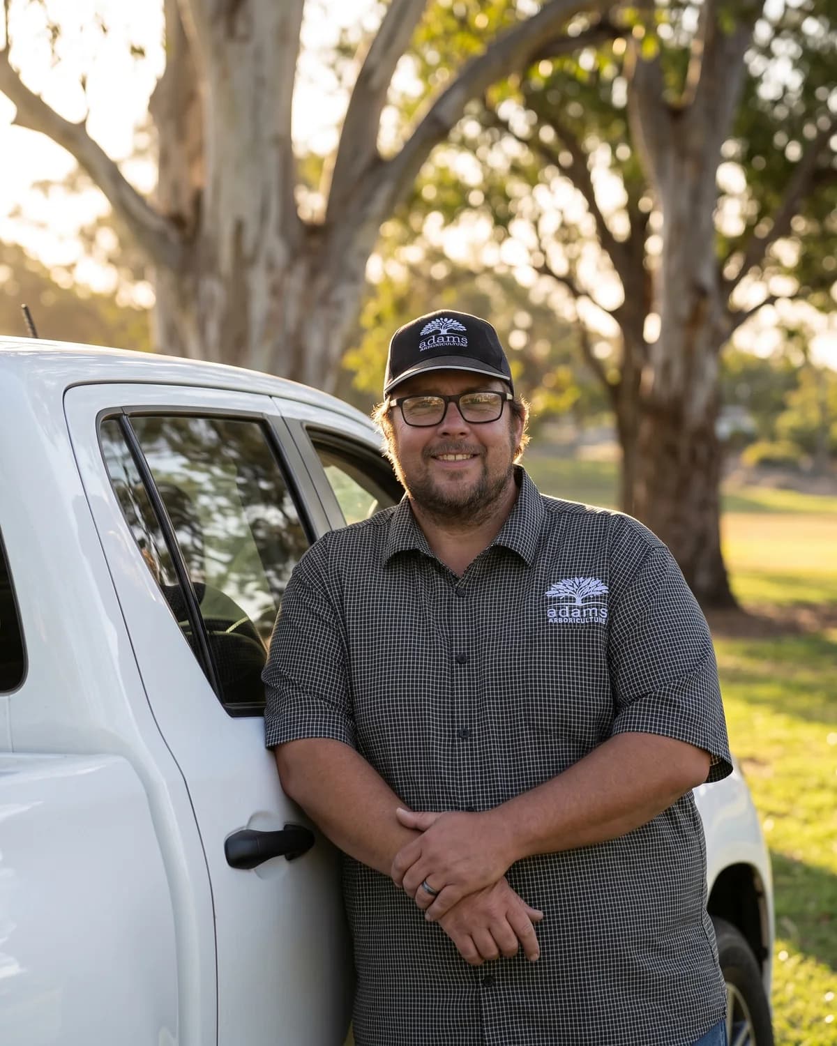 Adam De Regt, consulting arborist, standing beside his work vehicle under mature eucalypts in late afternoon light