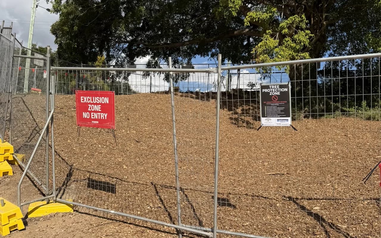 Temporary fencing and an exclusion zone sign enclosing a mulched tree protection area on a construction site